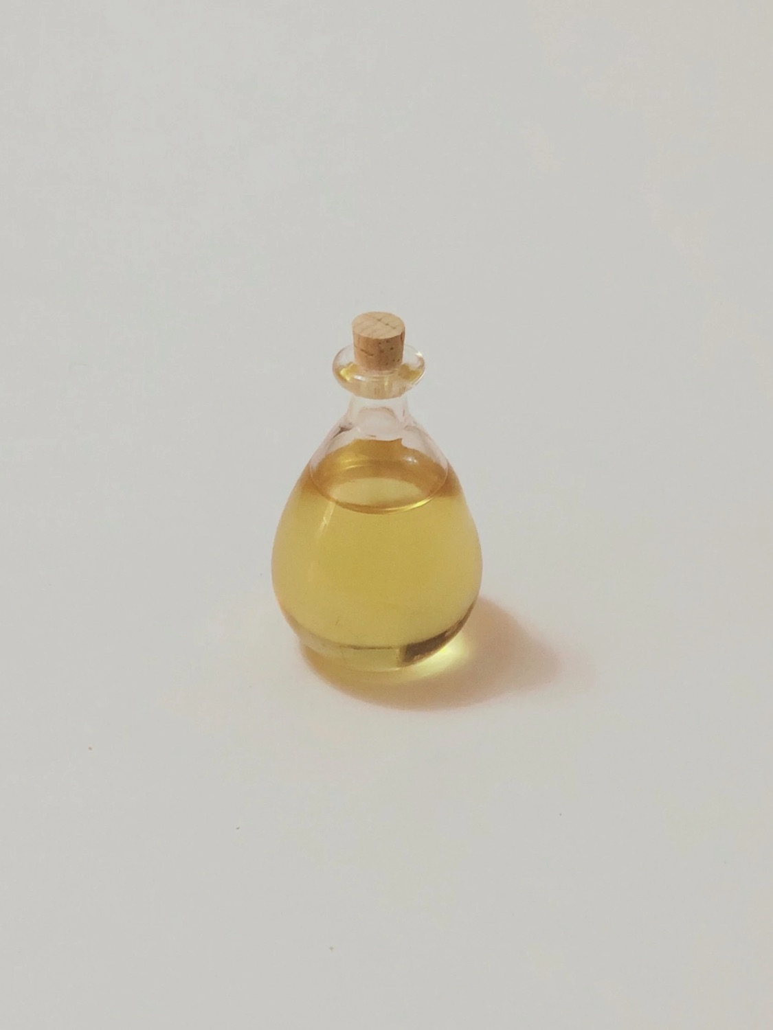 The finished oil: a small teardrop-shaped glass bottle of golden oil with a cork stopper, alone on a white surface.