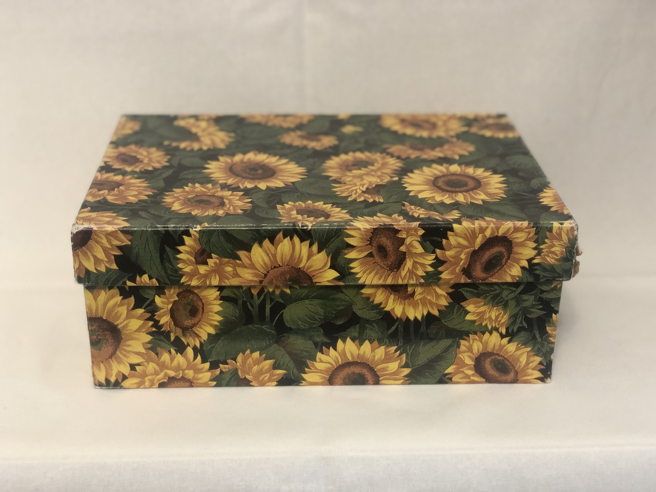A closed keepsake box covered in sunflower-print paper, its corners worn, on a plain cloth.